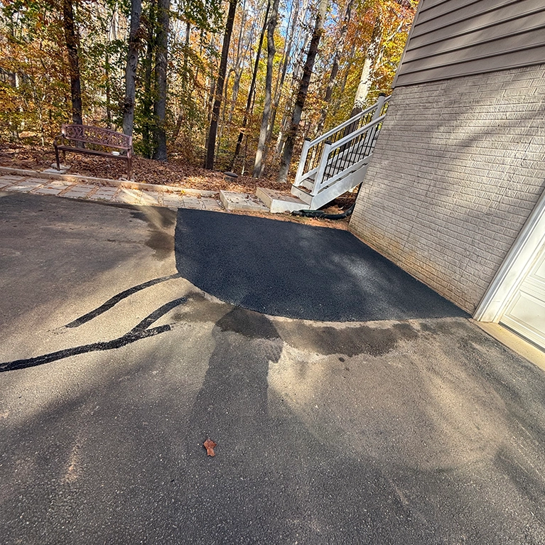 Freshly paved asphalt area next to a garage, with a stairway in the background and a wooden bench amid autumn foliage. Freshly paved asphalt area next to a garage, with a stairway in the background and a wooden bench amid autumn foliage.